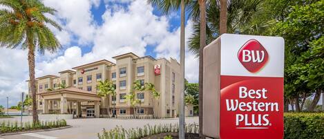 A Best Western Plus hotel with a modern facade, palm trees, and a clear sky.