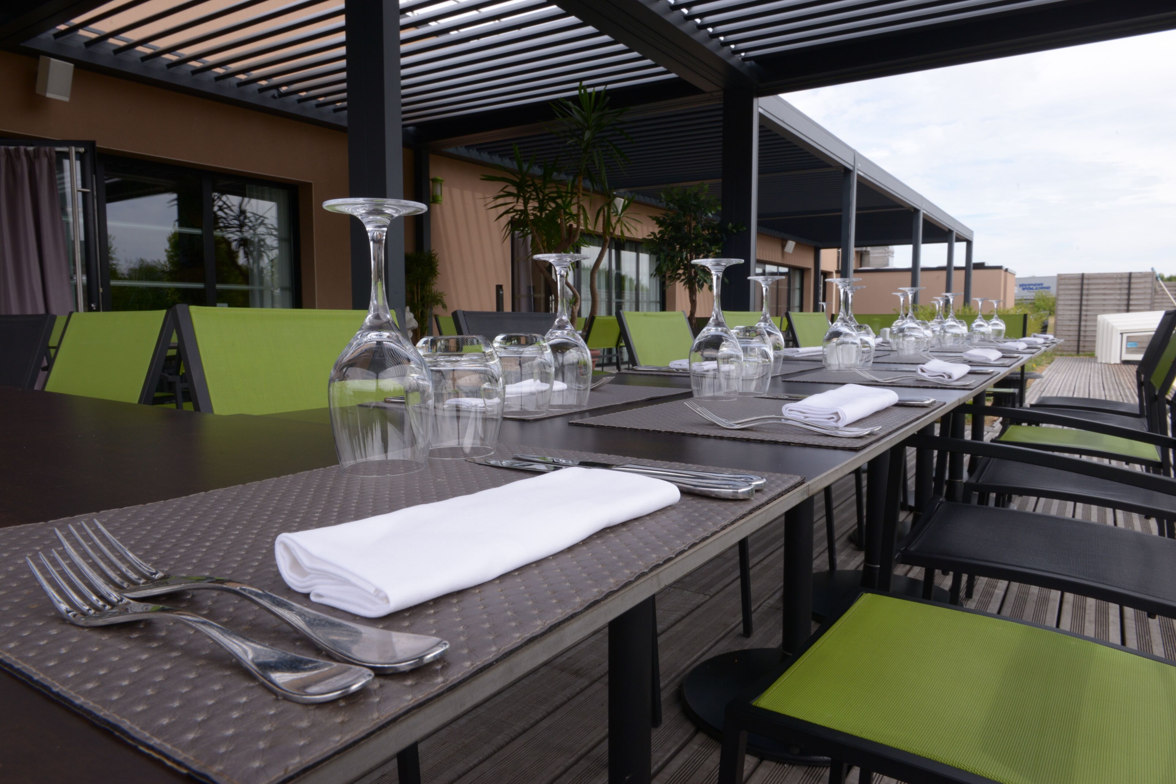 A covered outdoor dining area with tables set for two, featuring clear glassware and neatly folded white napkins.
