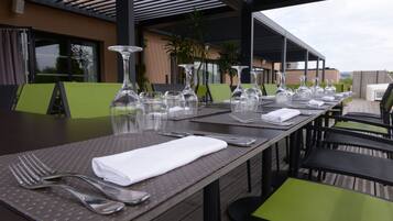 A covered outdoor dining area with tables set for two, featuring clear glassware and neatly folded white napkins.