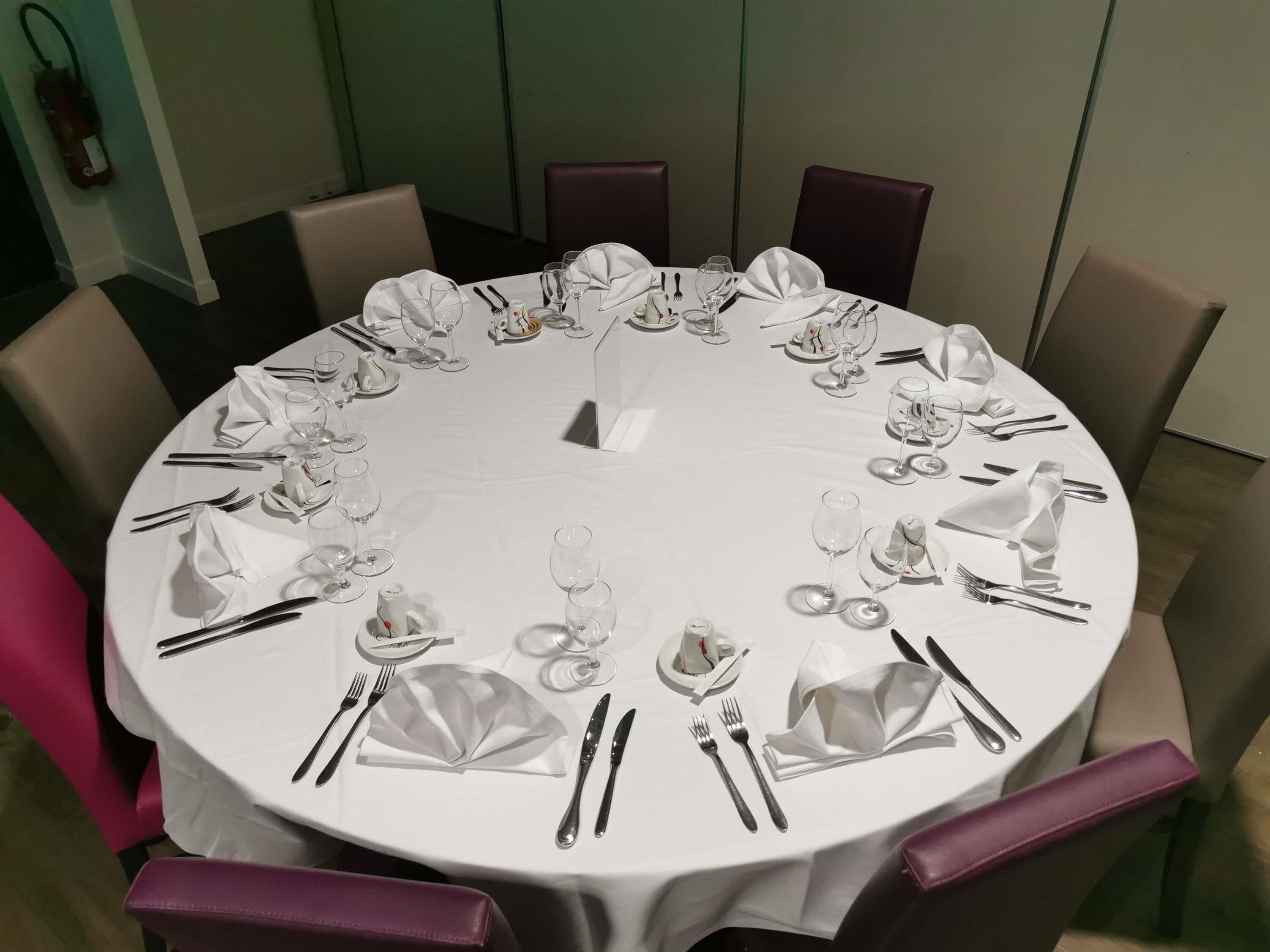Une table ronde dressée pour un repas, avec des nappes blanches, des couverts en argent et de la verrerie.