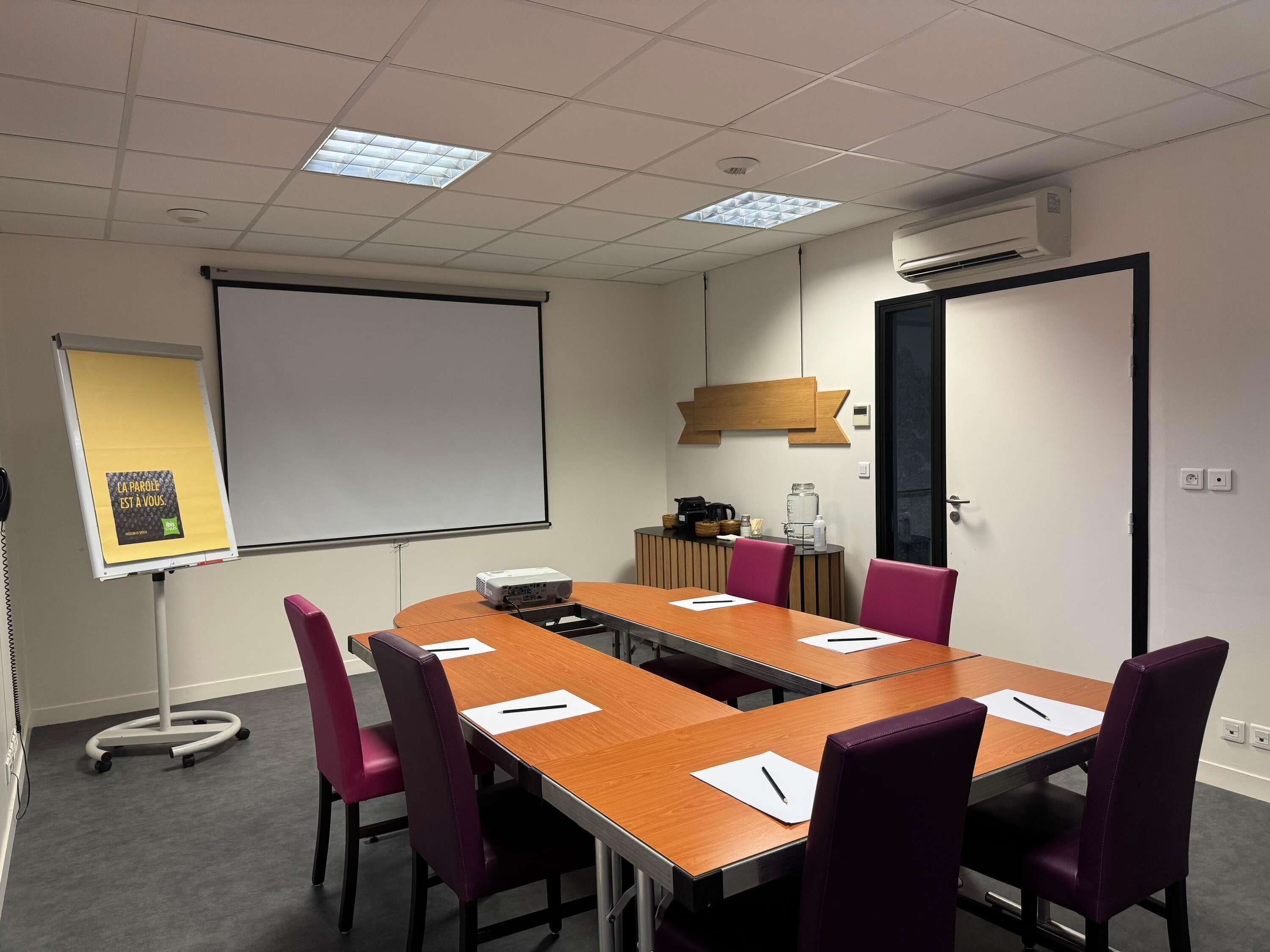 A conference room with a long table, chairs, a projector, and a screen.