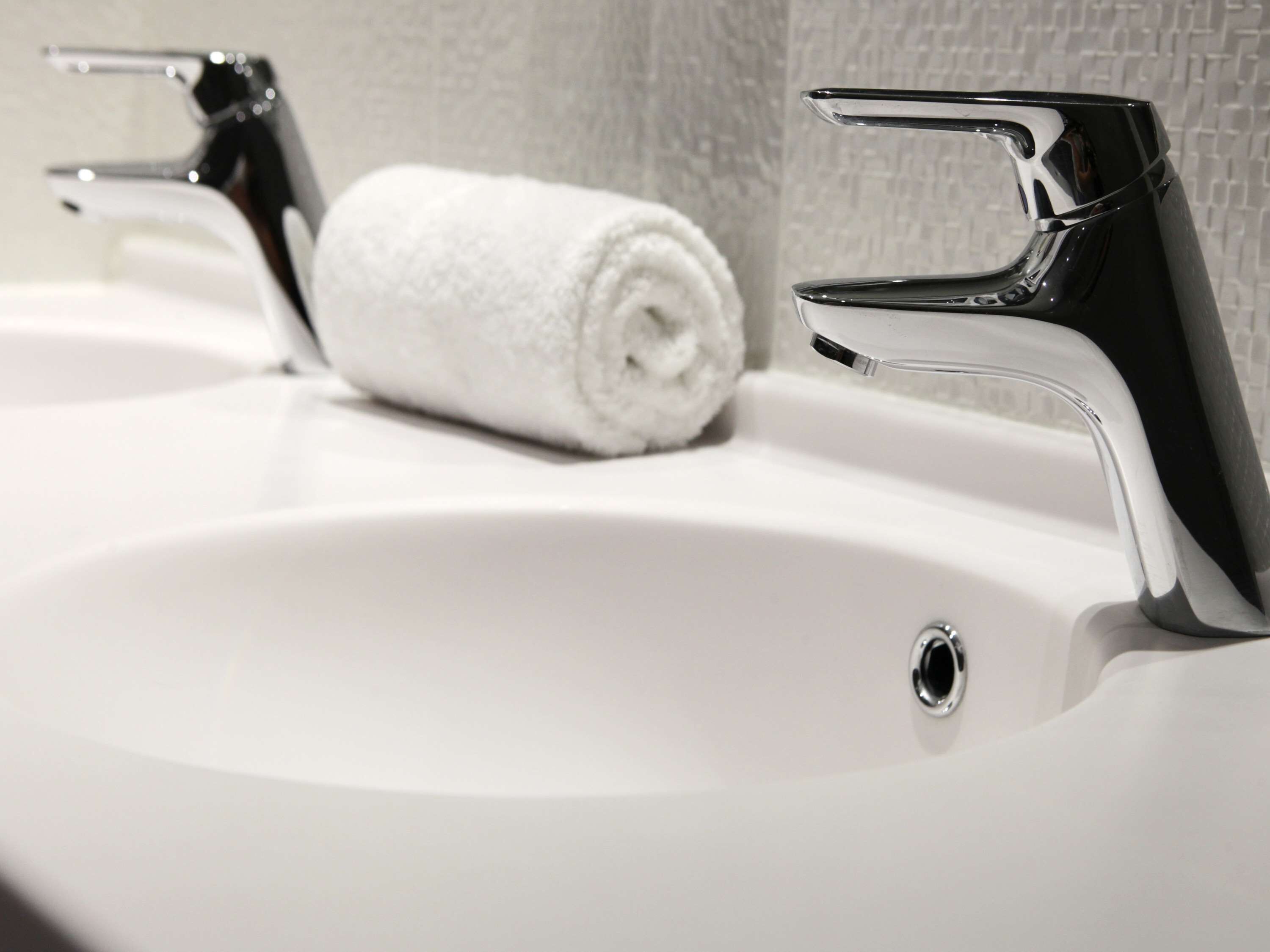 Un lavamanos blanco con grifos cromados y una toalla blanca enrollada.