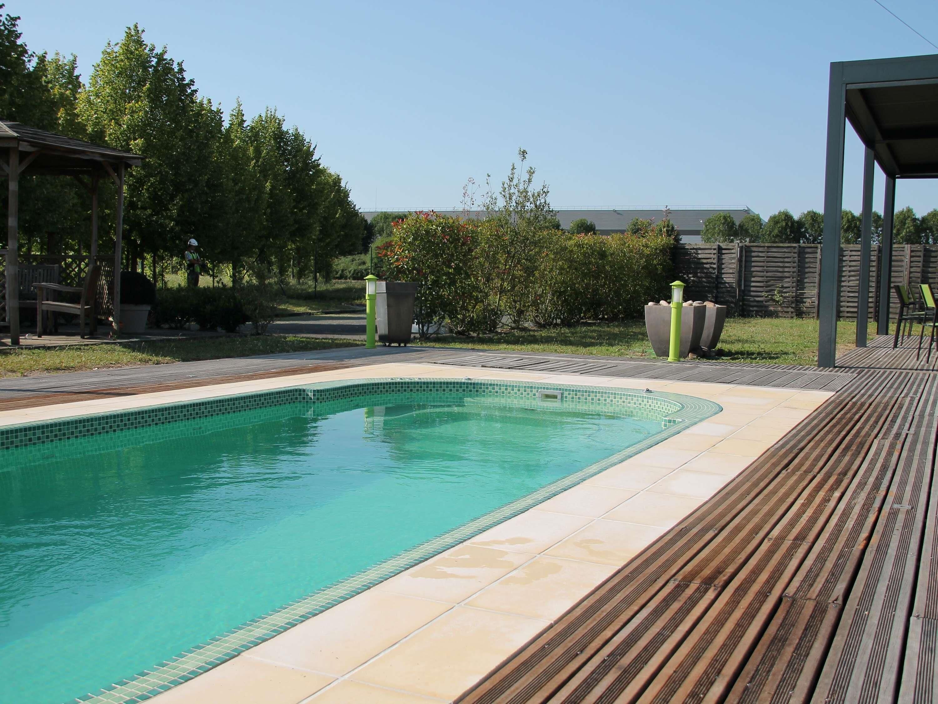 A rectangular swimming pool with a tiled edge, surrounded by a wooden deck.