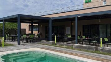A hotel with outdoor seating, a swimming pool, and a sign for 'ibis Styles Hotels'.
