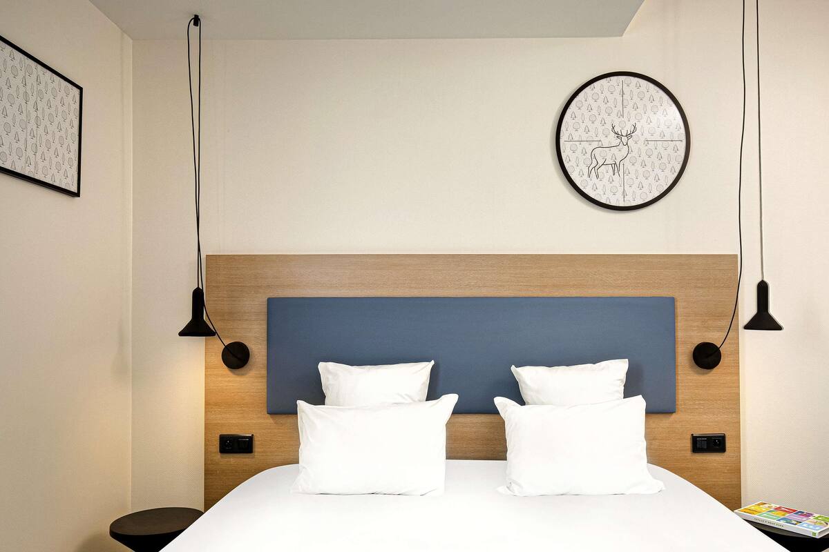 Un lit bien fait, avec du linge de lit blanc, une tête de lit en bois et une horloge fixée au mur.