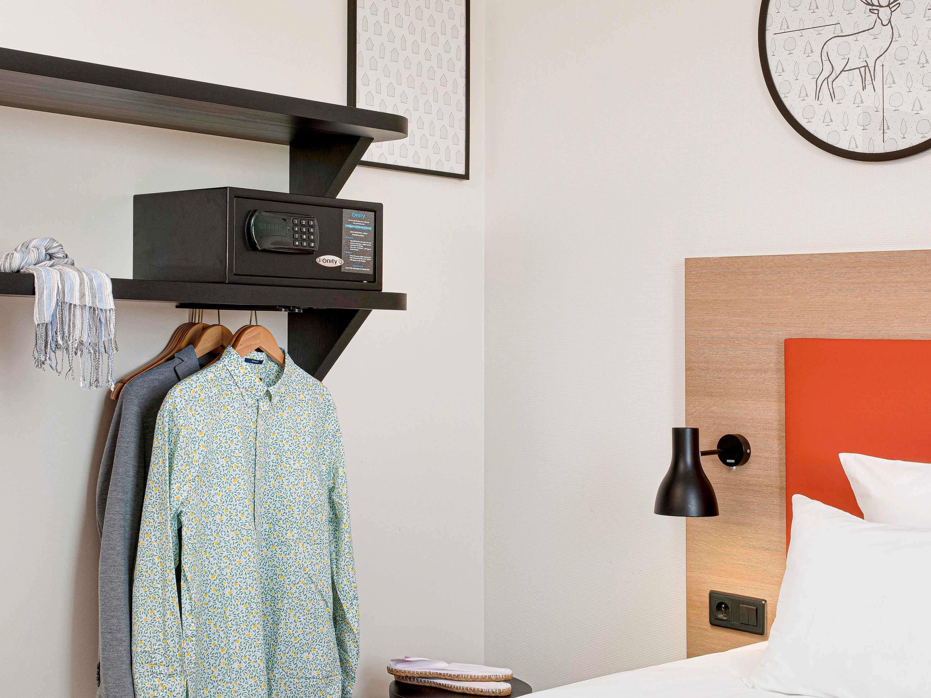 A hotel room with a bed, a bedside table, a lamp, a radio, and a wall clock.