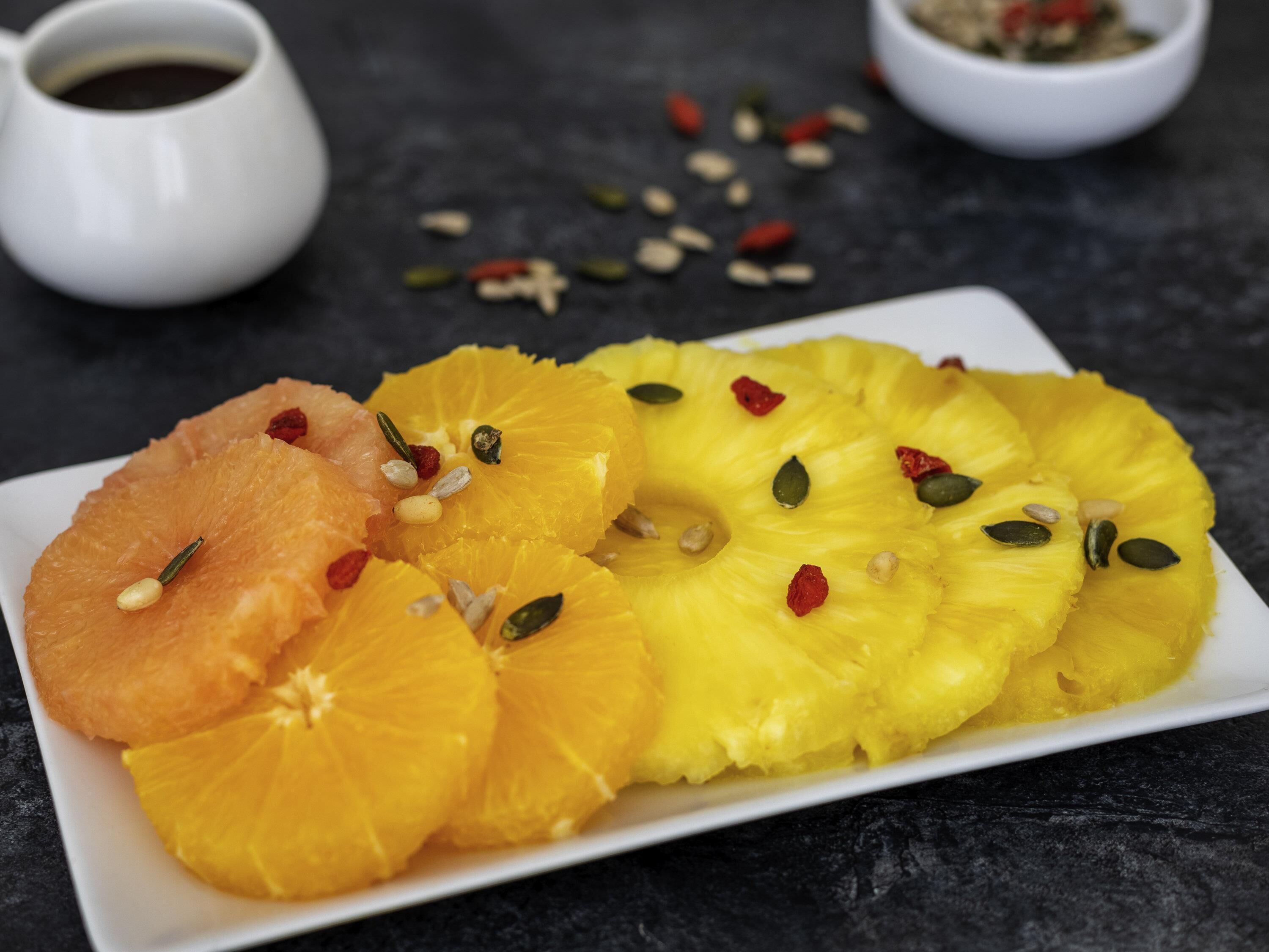 Un plato de frutas cortadas con semillas y frutas deshidratadas sobre una superficie oscura.