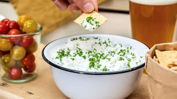 A bowl of white dip garnished with herbs, a glass of beer, and a container of olives.