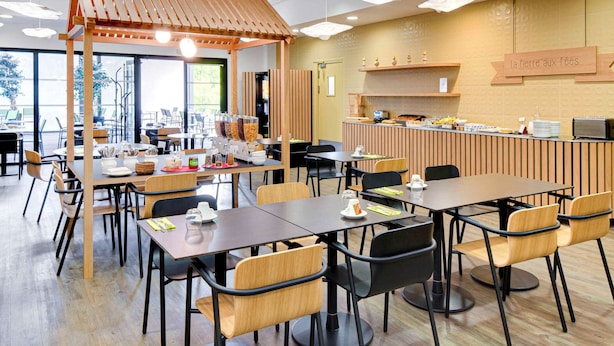 A modern cafe with wooden furniture, a counter with food items, and a sign reading "La Pierre aux Fées".