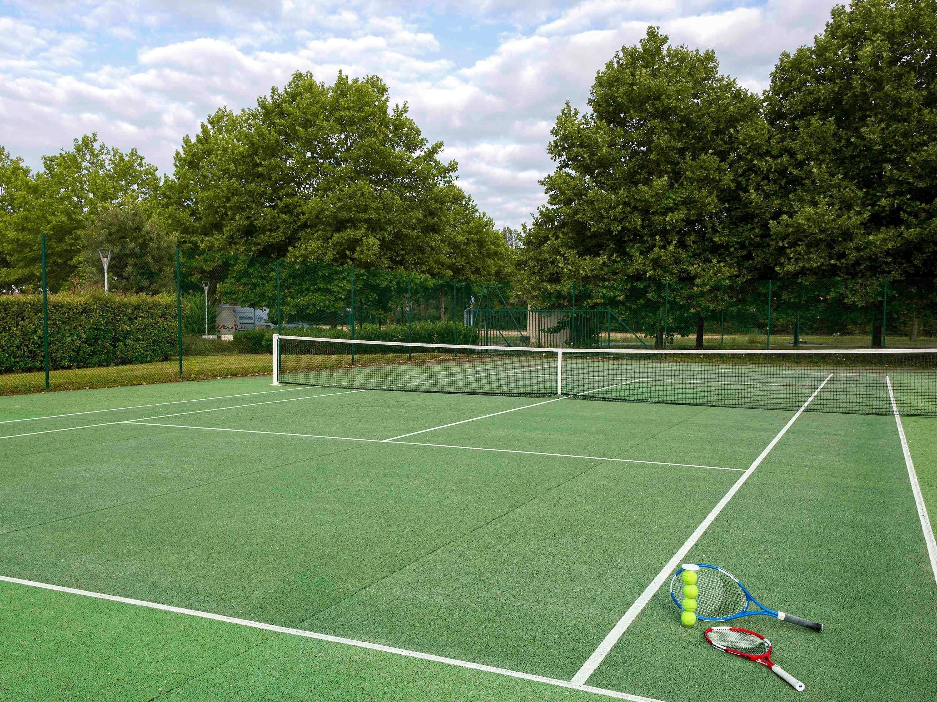 A tennis court with a net, green surface, and tennis rackets.