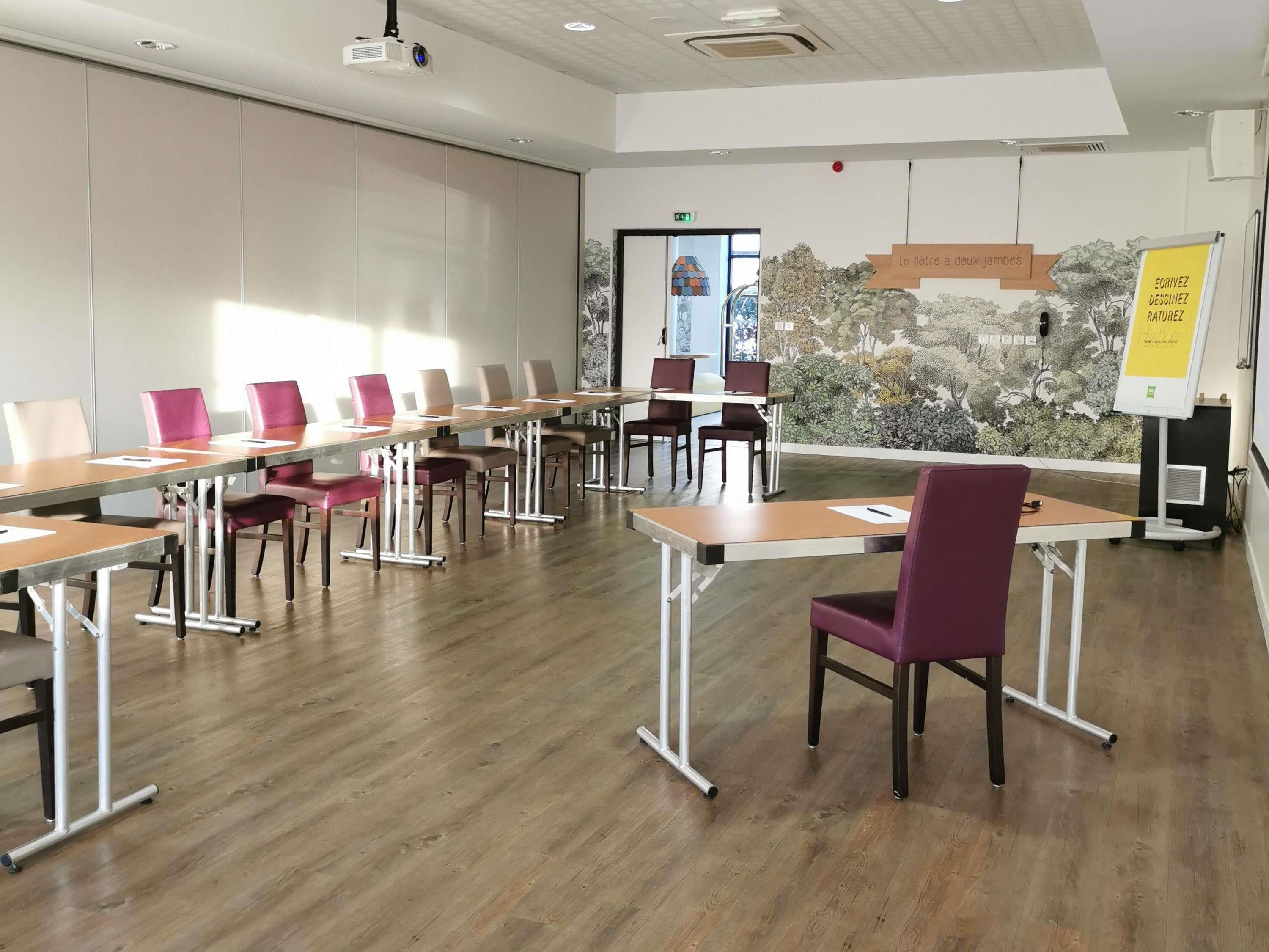Un salón de conferencias con una larga mesa, sillas, un proyector y una pizarra.