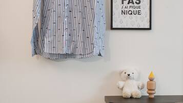 A room with a striped shirt hanging on the wall, a framed quote, a teddy bear, a small table with a book, a blue ottoman, and a chair.