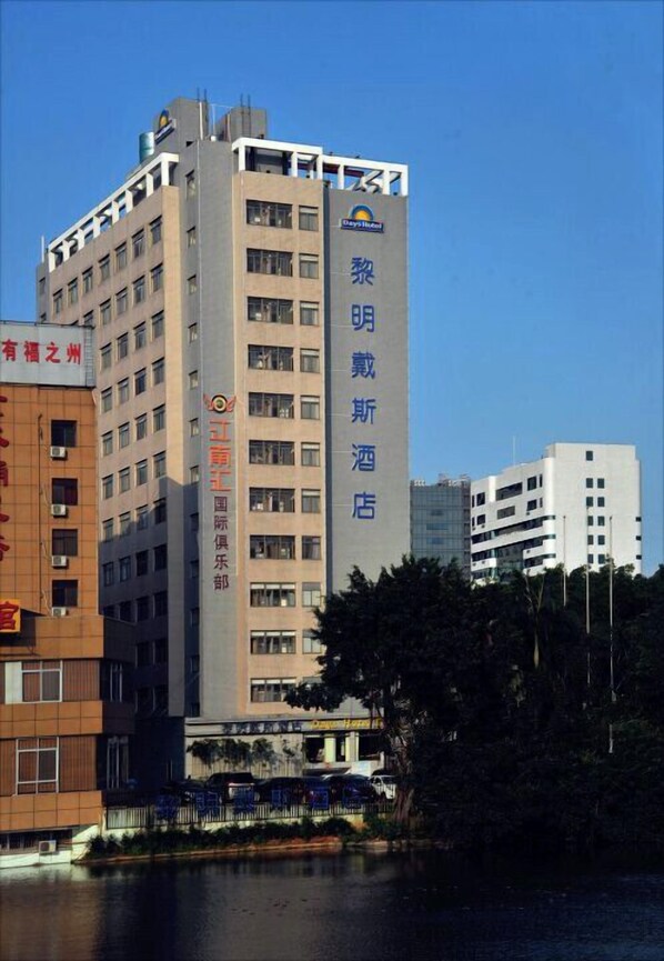 A hotel building with multiple floors, a prominent vertical sign with text, and a body of water in the foreground. - Days Hotel Dawn Fuzhou (Fuzhou)