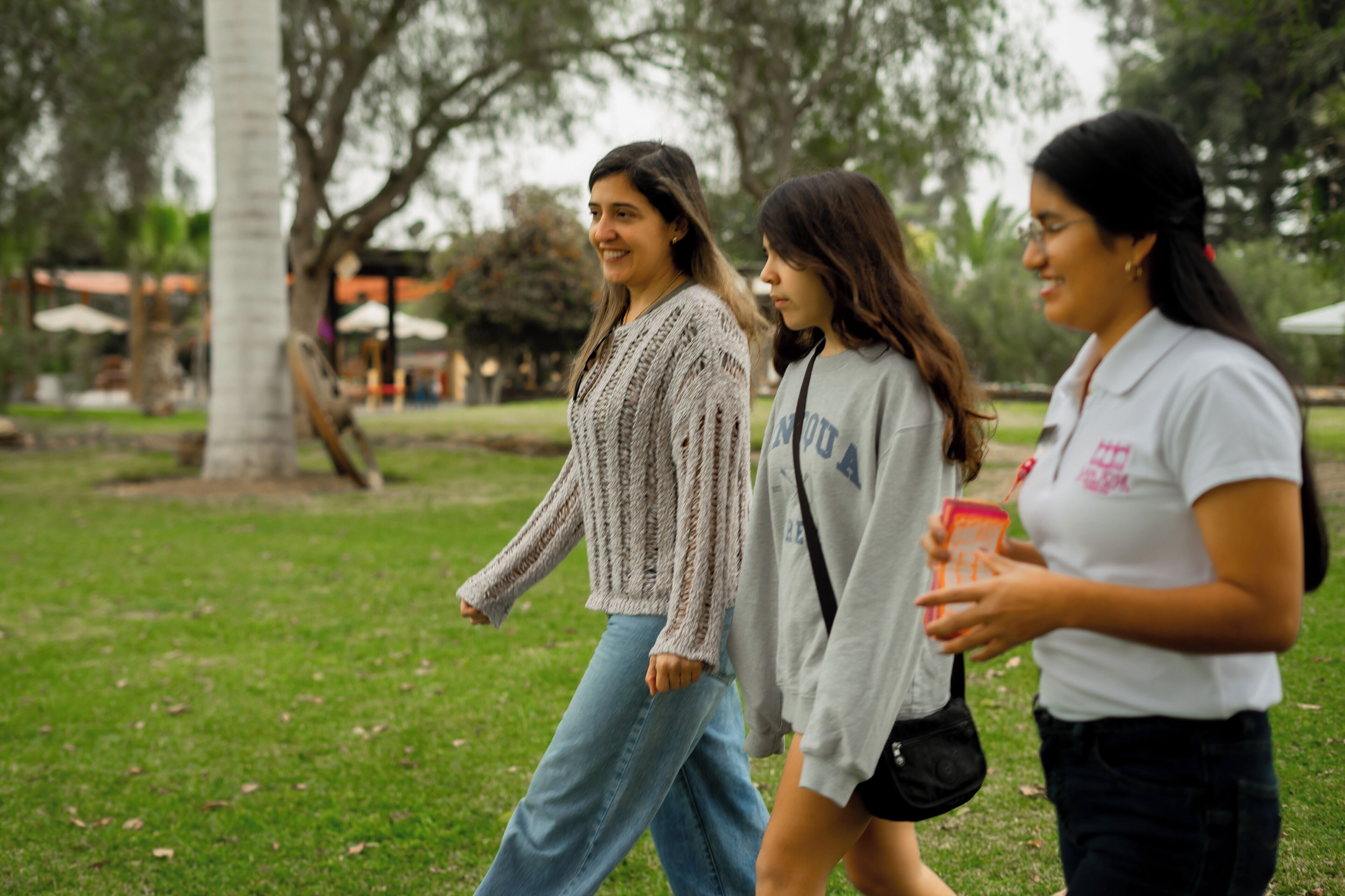 Tres persones caminant a un parc amb gespa i arbres.