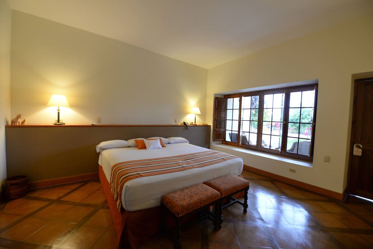 Een slaapkamer met een groot bed, twee bedlampen, een raam met uitzicht en een houten bankje.