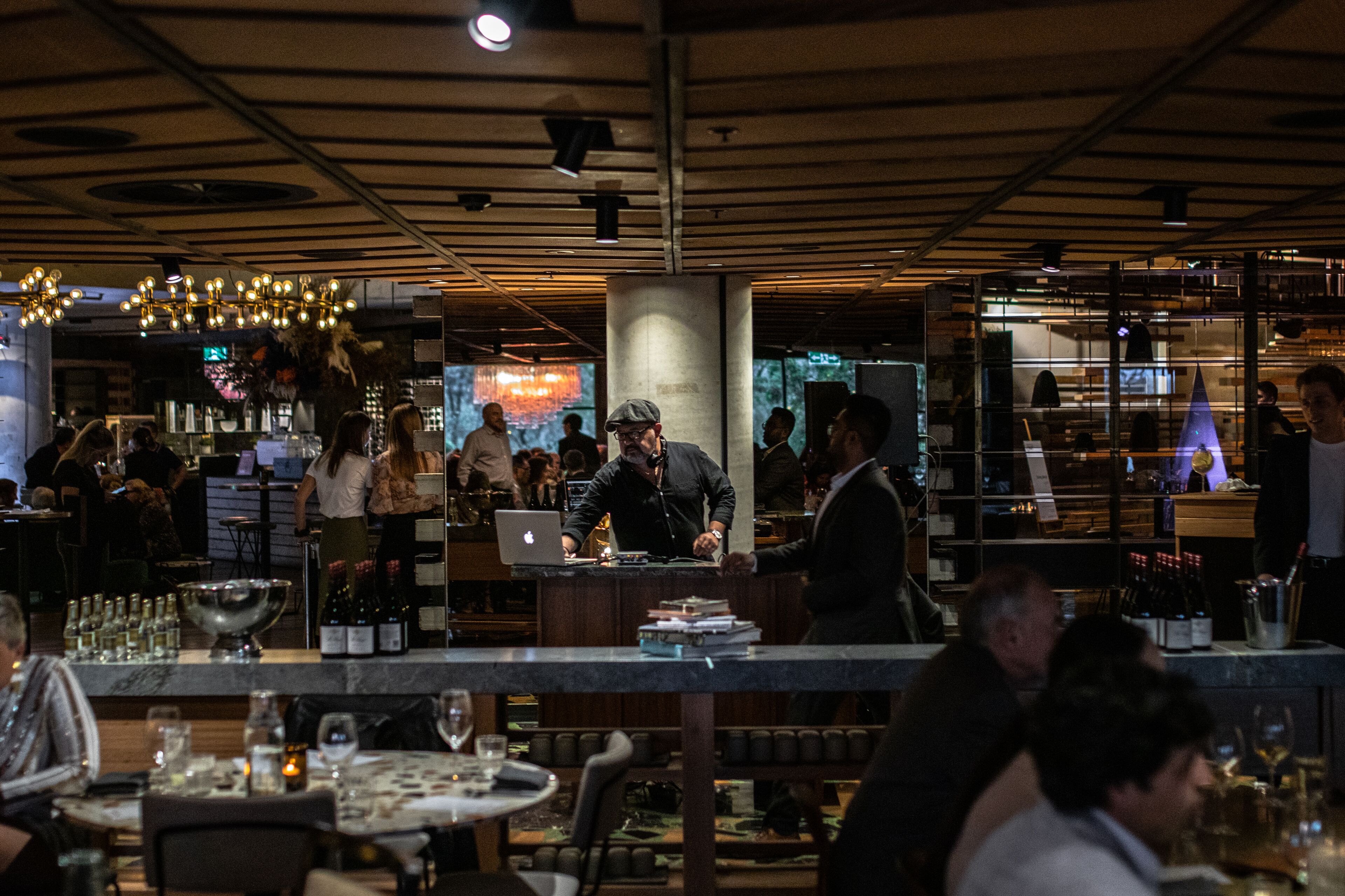A modern restaurant interior with a bar area, dining tables, and a bartender.