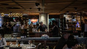 A modern restaurant interior with a bar area, dining tables, and a bartender.