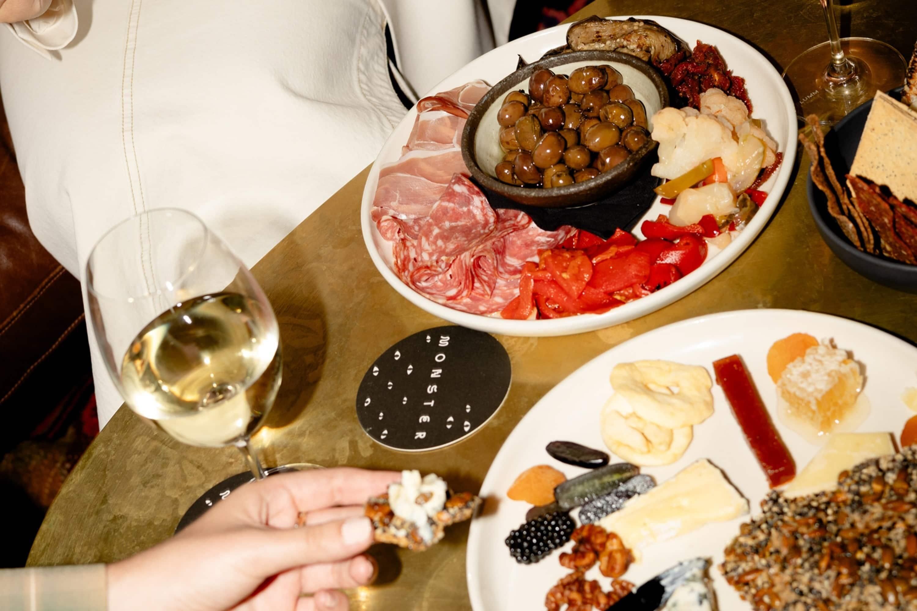 A table with various food items, including meats, cheeses, and olives, and a glass of white wine.