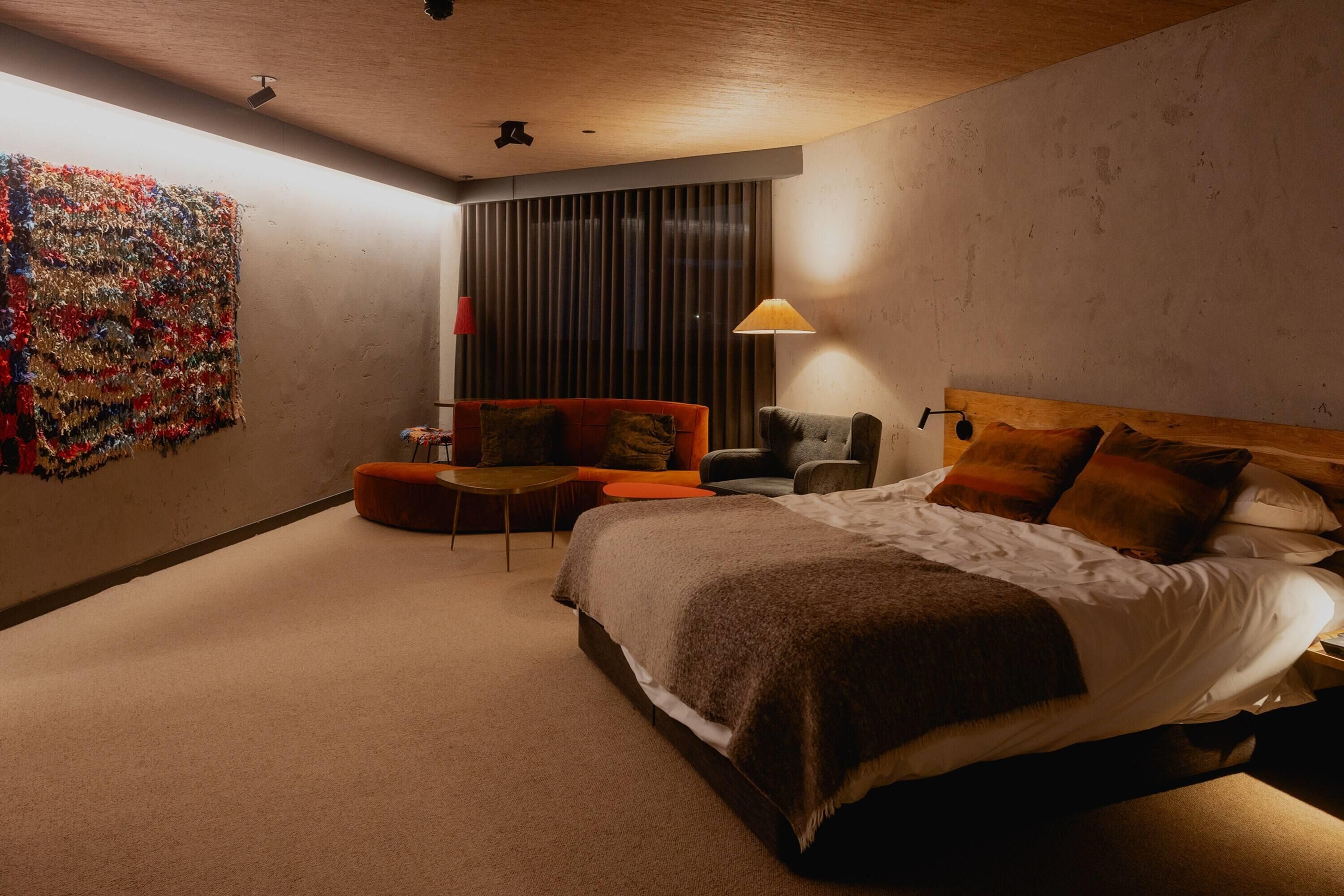 Quarto de hotel moderno com uma cama grande, um sofá, uma cadeira e uma mesinha.