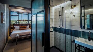 Een moderne hotelkamer met een bed, een douche, een wastafel en een groot raam.