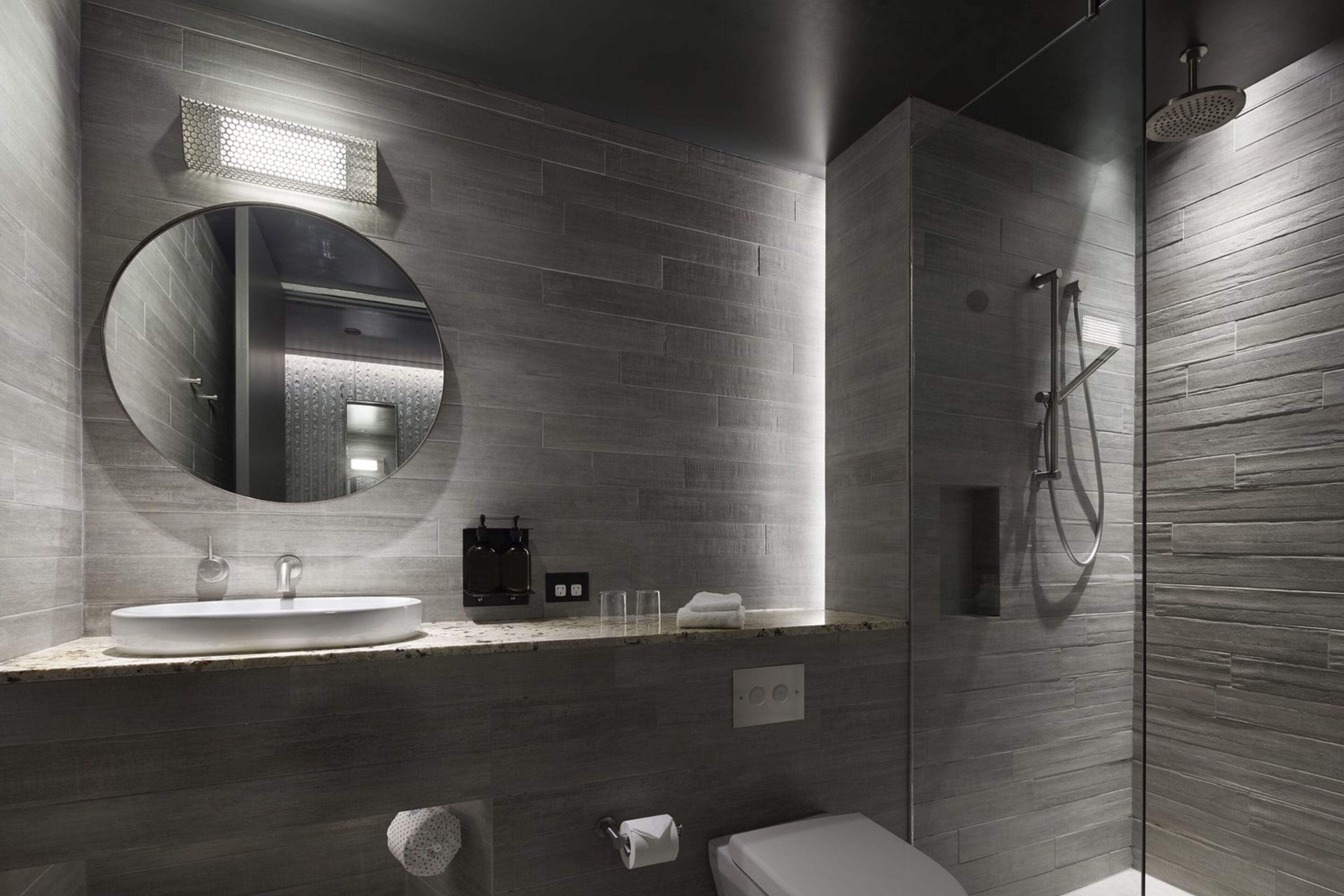 Une salle de bain moderne avec un grand miroir rond, un lavabo et une douche à parois de verre.