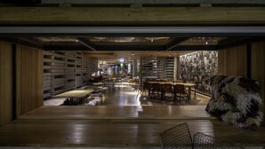 A modern interior with wooden flooring, a central seating area with tables and chairs, and a wall displaying various items. - Ovolo Canberra, a Wyndham Hotel (Canberra)