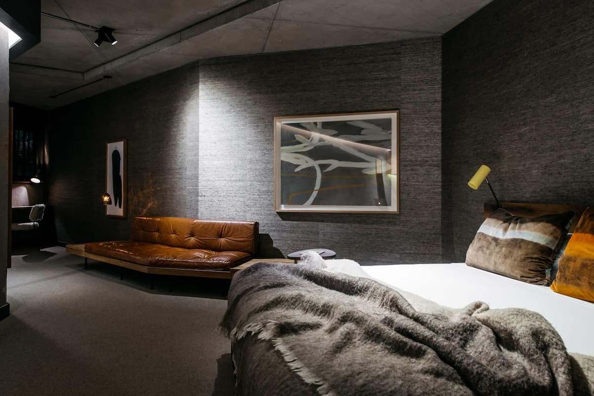 Un dormitorio moderno con cama, sofá de cuero y un cuadro abstracto grande en la pared.