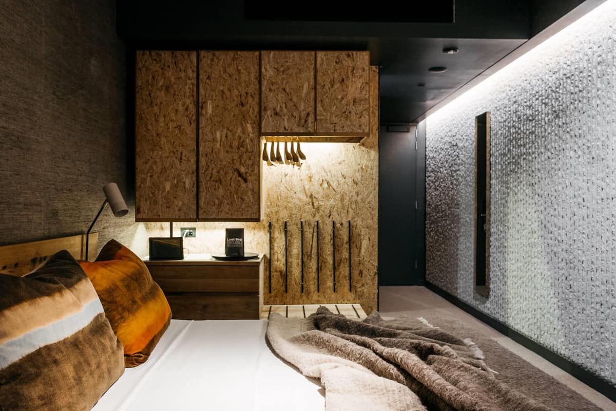 Un dormitorio moderno con cabecera de madera, una mesita de noche con lámpara y una cama grande con manta.