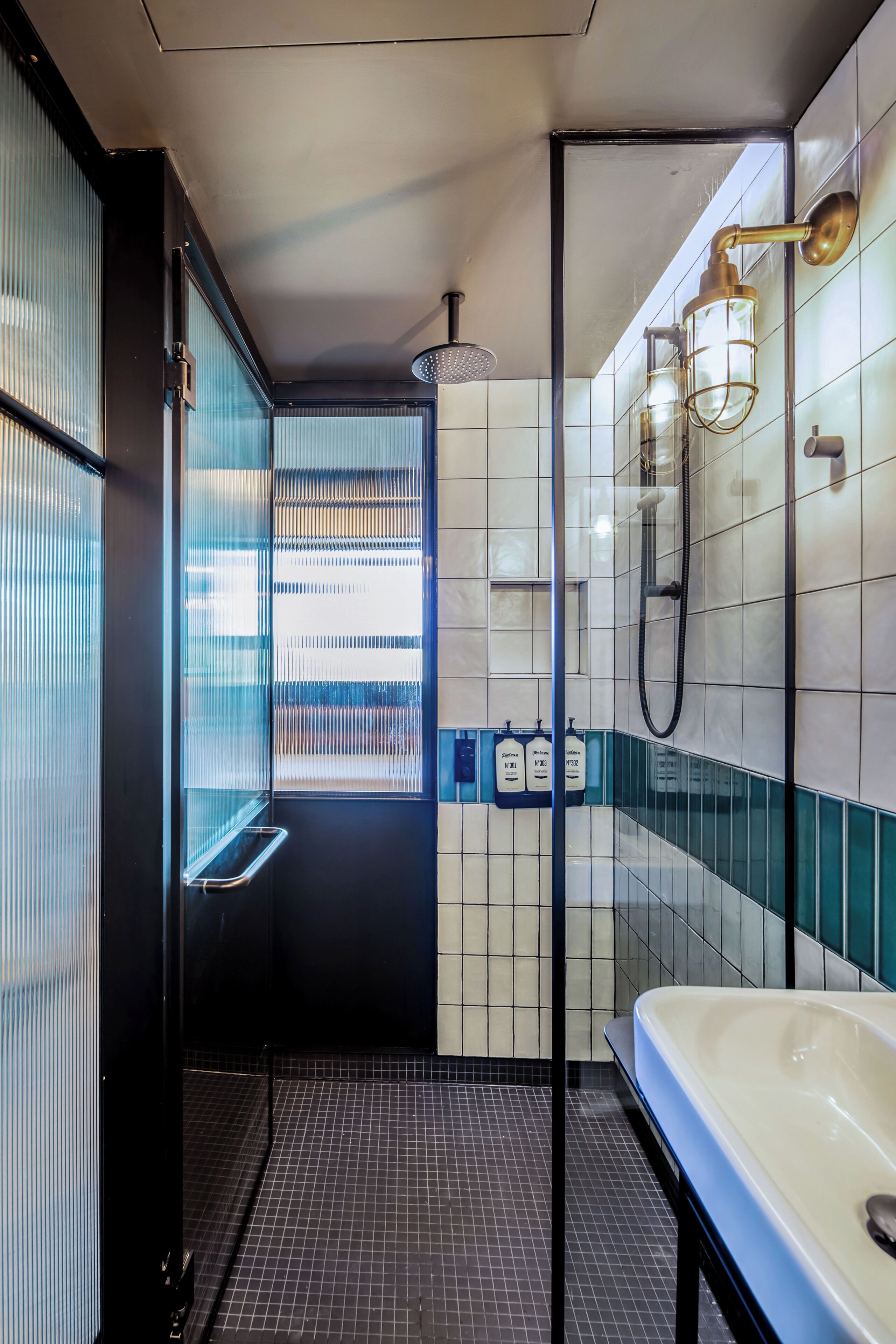 Un baño moderno con mampara de vidrio, una bañera blanca y un revestimiento de azulejos con detalles azules.