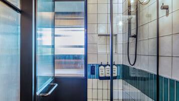 Moderni kylpyhuone, jossa on lasinen suihkuseinä, valkoinen kylpyamme ja sinisillä yksityiskohdilla koristeltu laattaseinä.