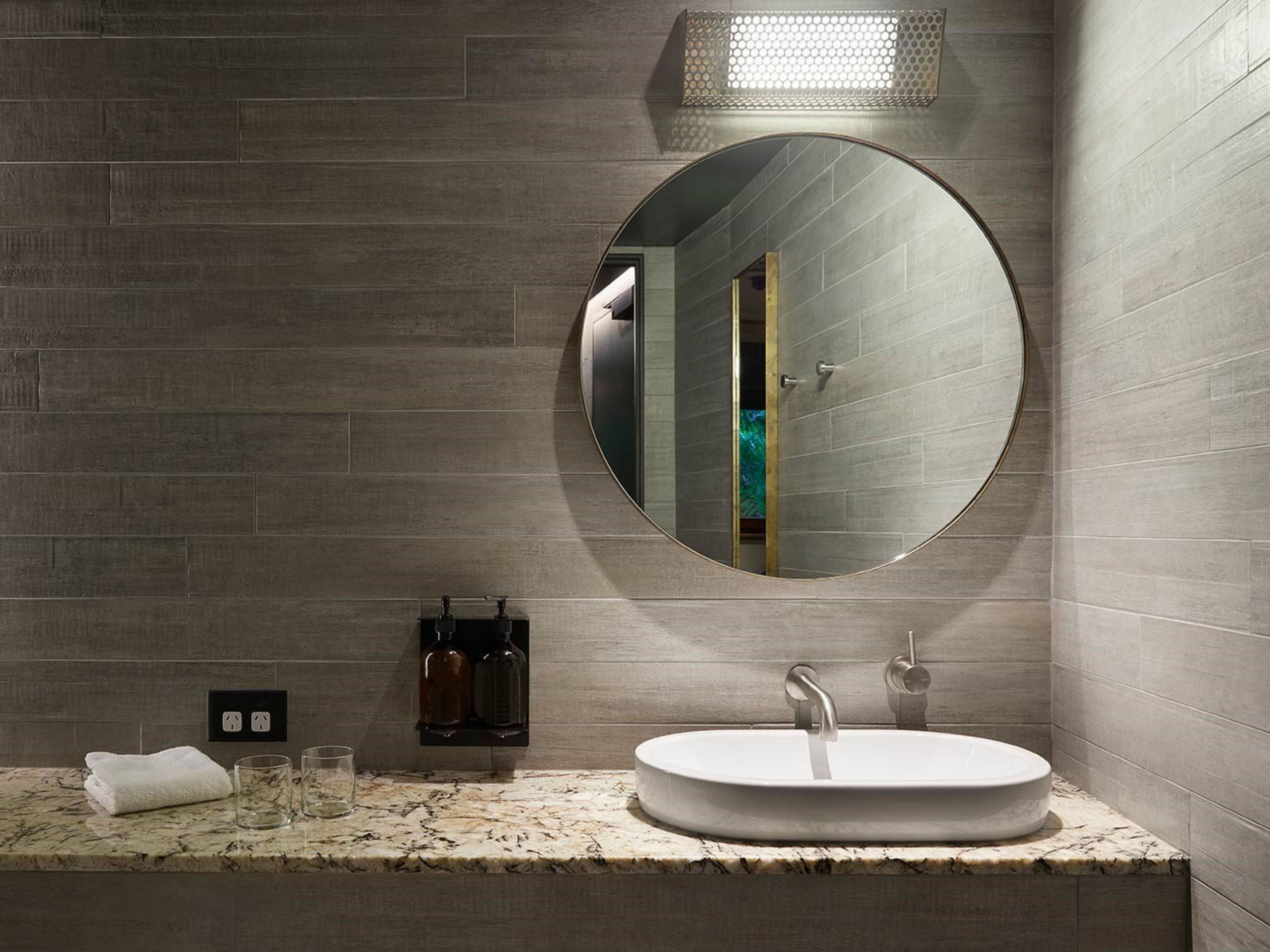 Une salle de bain moderne avec un miroir rond, un lavabo blanc et un plan de toilette en marbre.