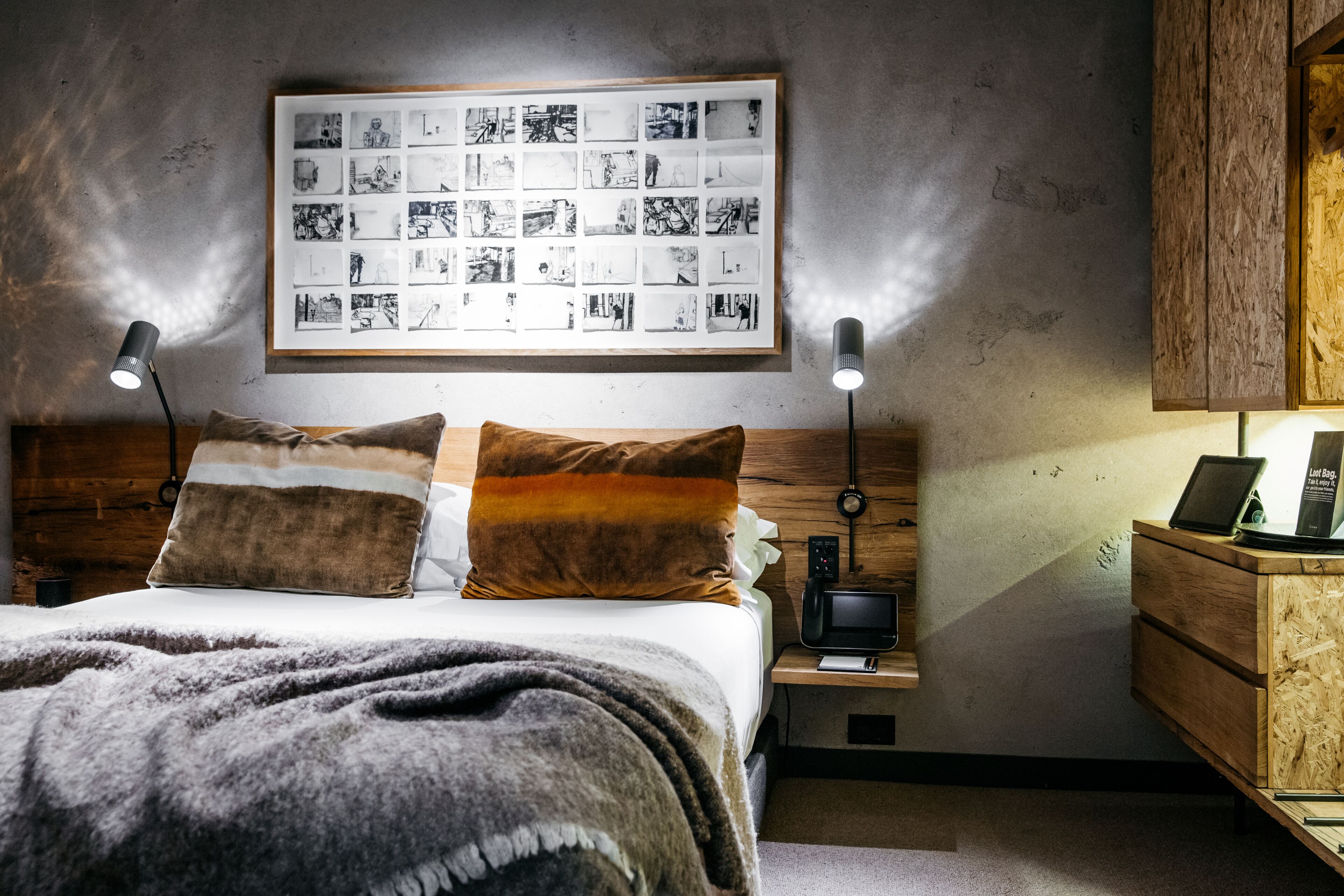 Een moderne slaapkamer met een houten hoofdbord, een lijst met zwart-witfoto’s aan de muur, nachtlampen, een klein nachtkastje met een lamp en een houten nachtkastje.