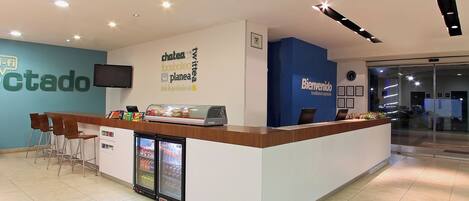 A reception desk with a blue accent wall, a television mounted above it, and a refrigerator with beverages.