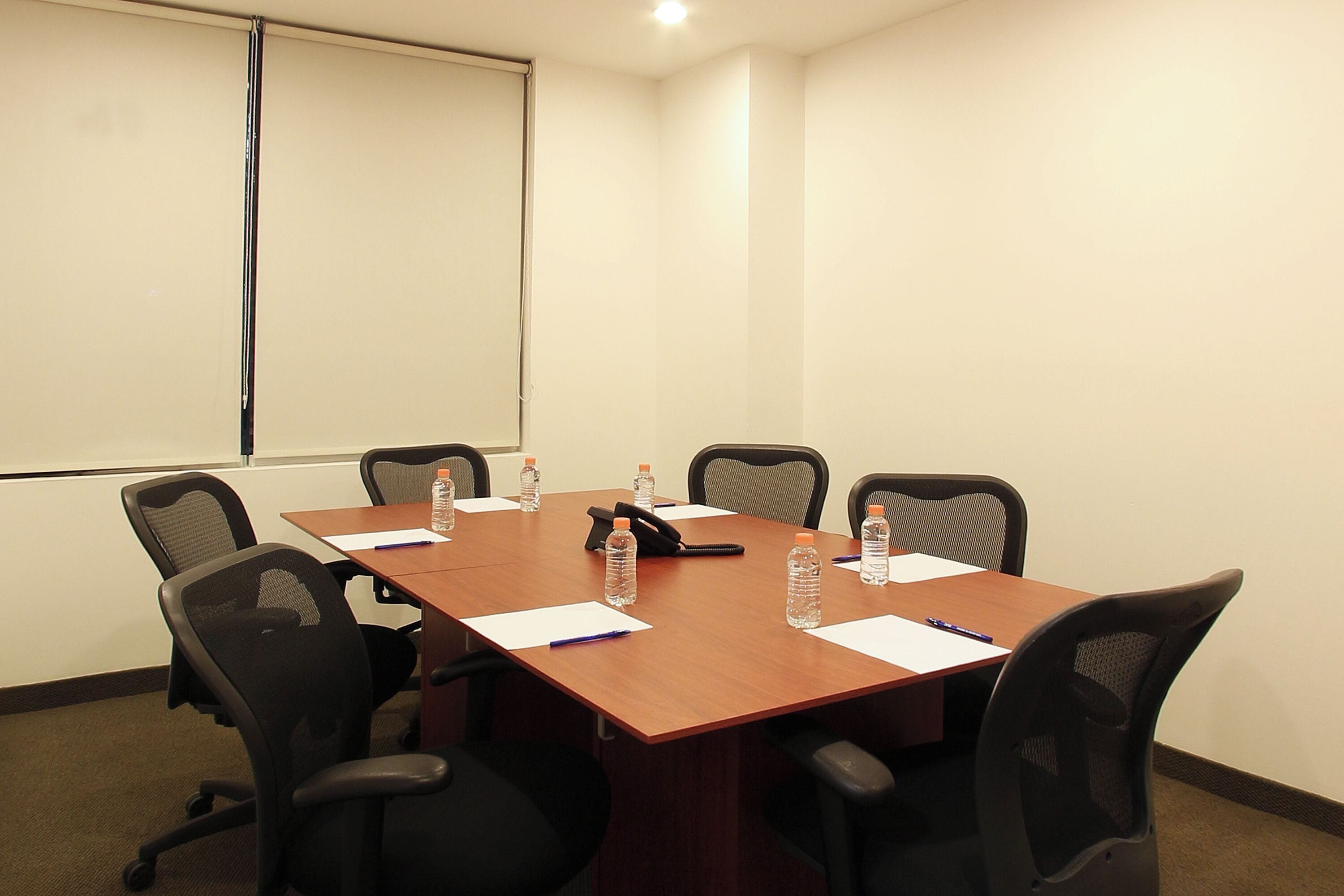 A conference room with a long table, six chairs, water bottles, papers, and a projector screen.