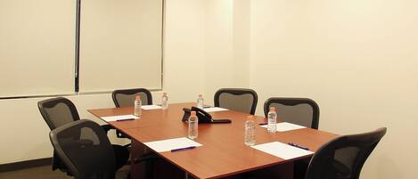A conference room with a long table, six chairs, water bottles, papers, and a projector screen.