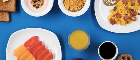 En frukostbuffé med rostat bröd, yoghurt, flingor, bönor, äggröra, korv, apelsinjuice, kaffe, äppelklyftor och bakverk.