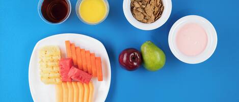 Un plato con frutas y verduras cortadas, dos manzanas y dos vasos de jugo sobre un fondo azul.