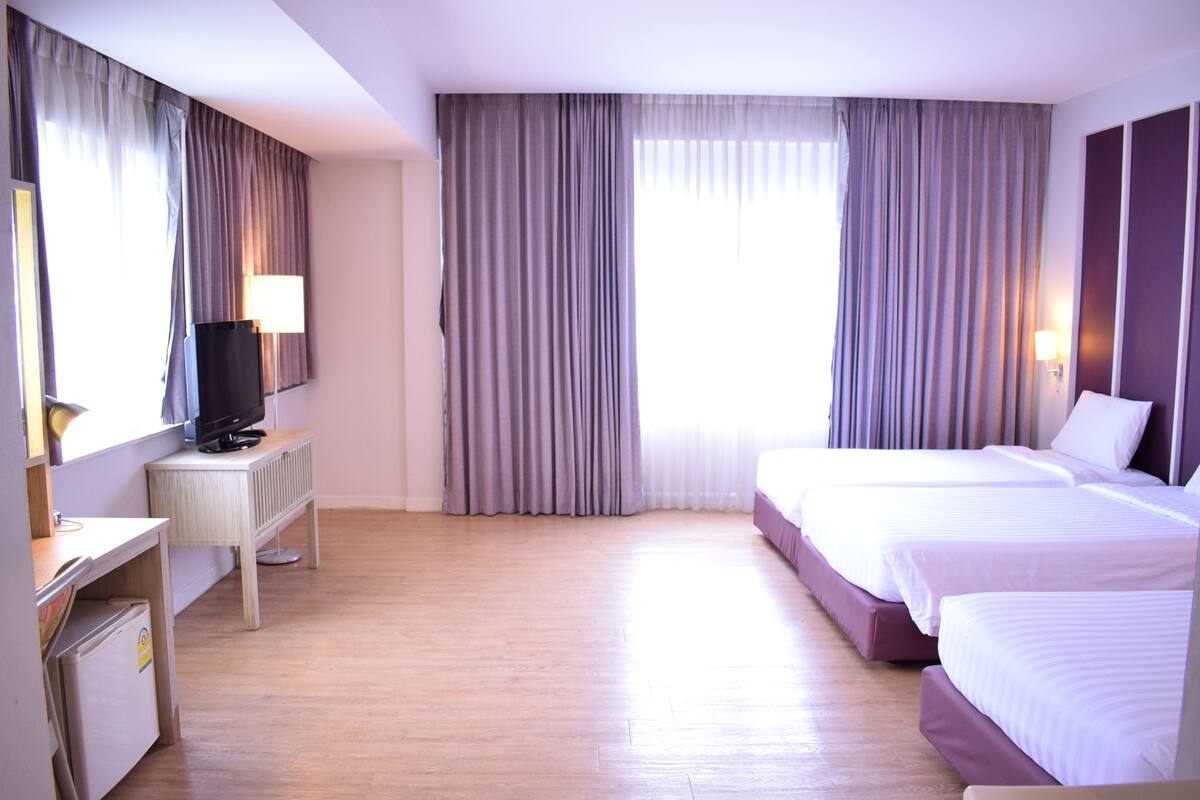 Une chambre d’hôtel avec deux lits, un bureau avec une télévision et des rideaux.