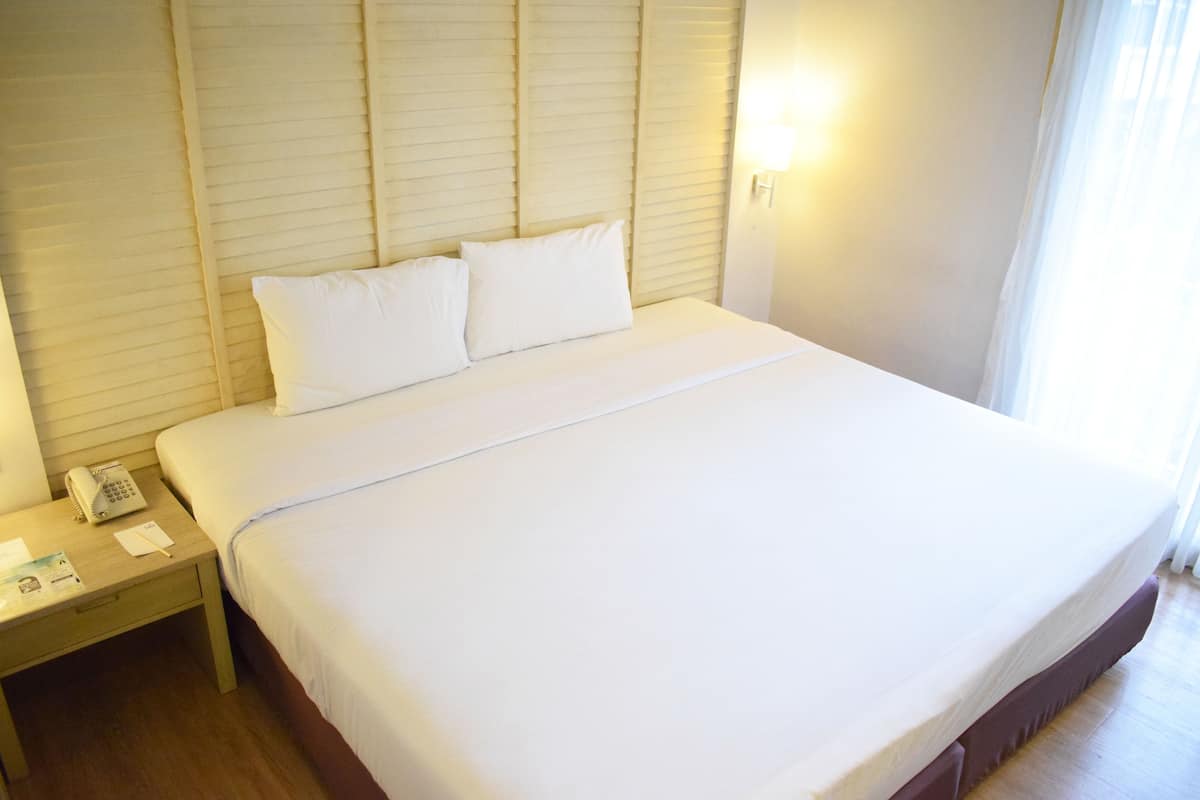Un lit bien fait, avec du linge de lit blanc, un téléphone sur la table de chevet et une petite table de nuit avec une lampe et des papiers.