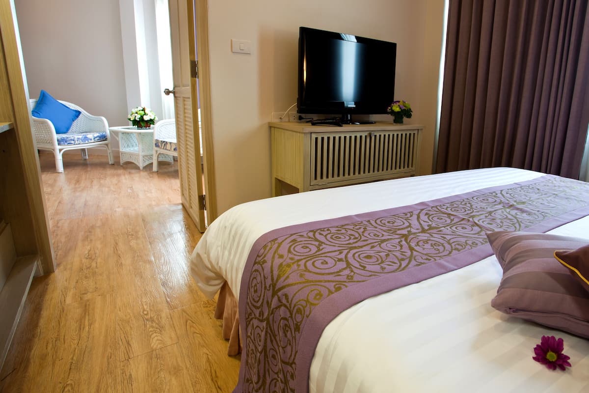 Une chambre d’hôtel avec un lit, un téléviseur posé sur un meuble, une petite table avec un vase de fleurs et une chaise.