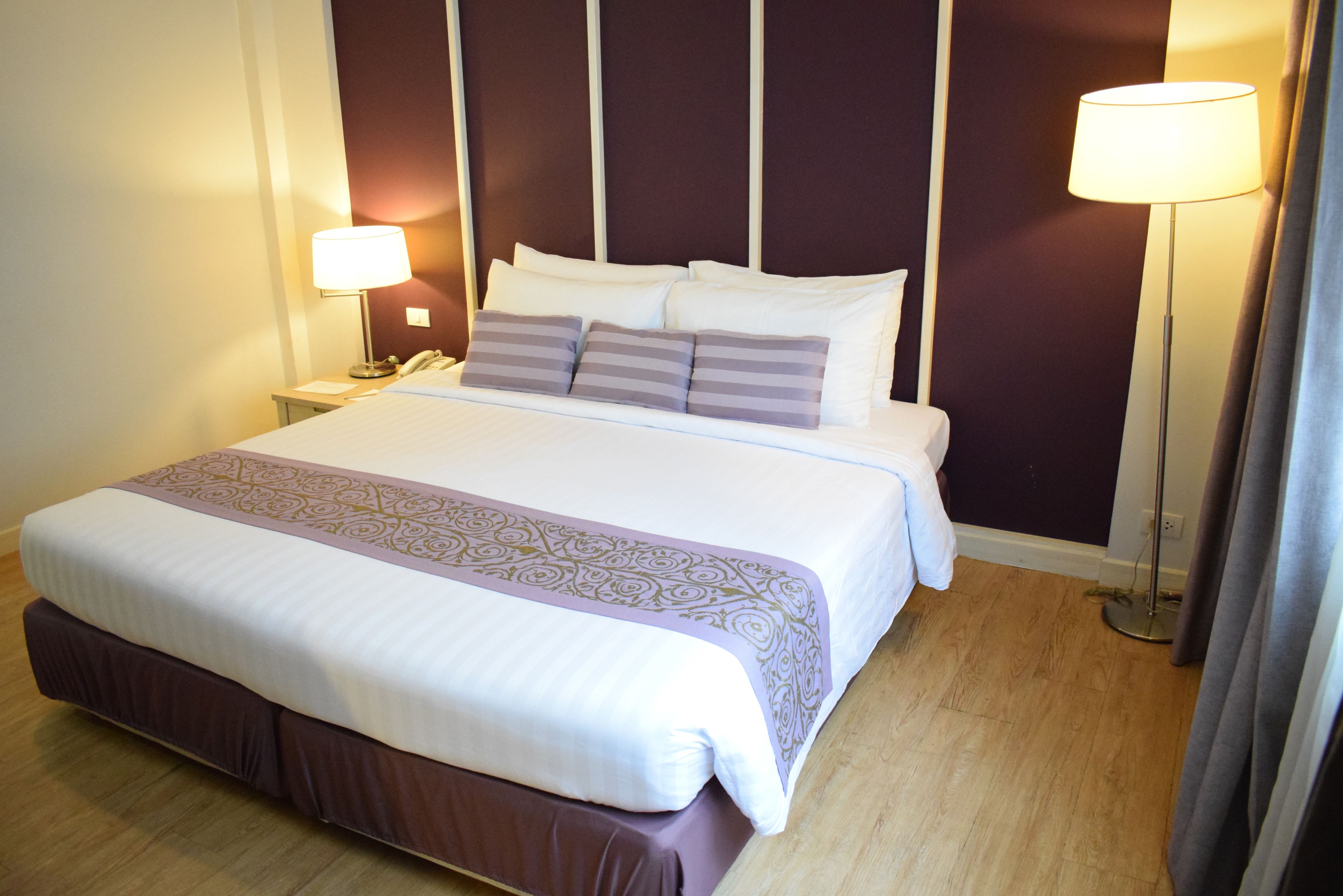 A neatly made bed with a patterned bedspread, two bedside lamps, and a nightstand with a phone.