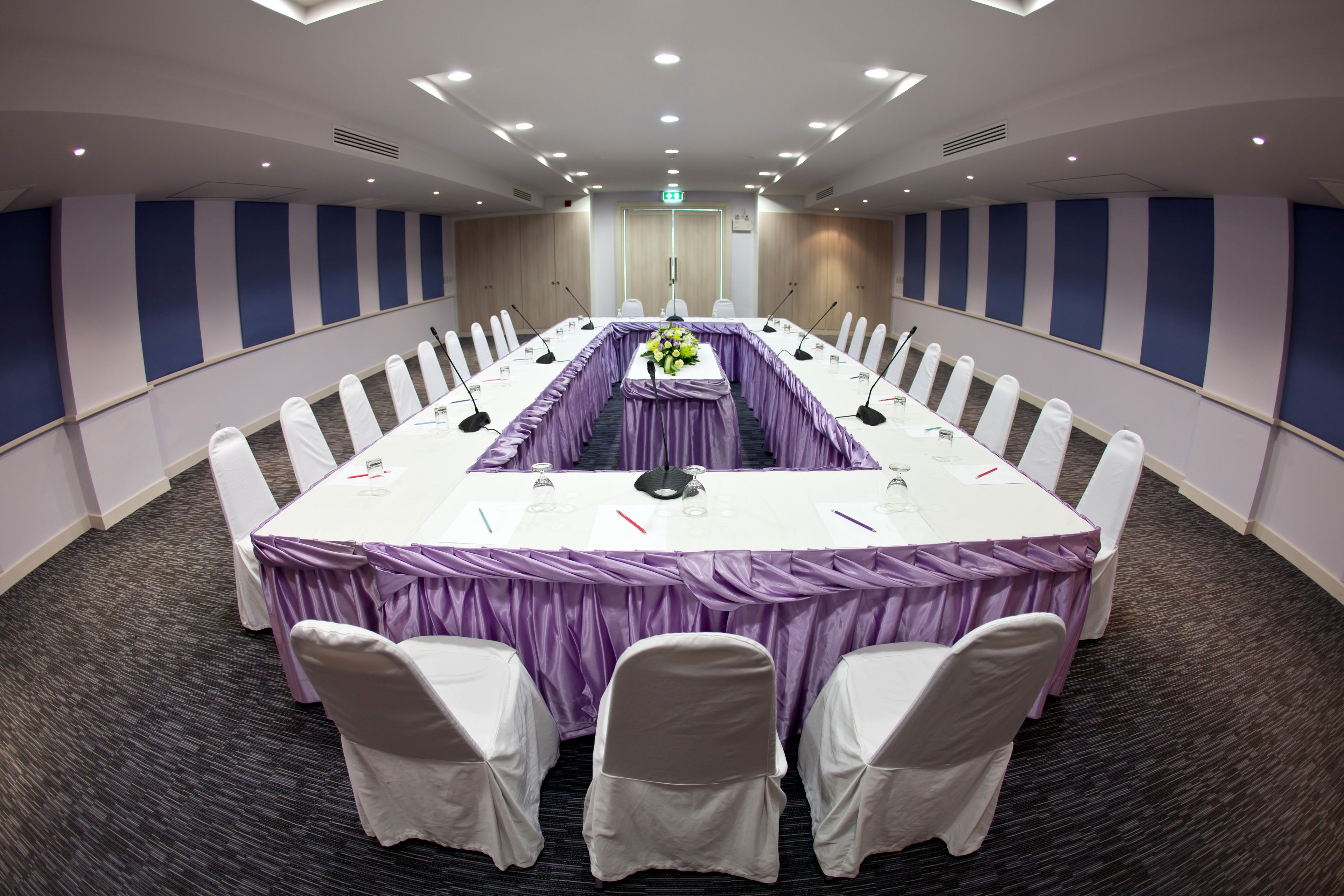 A conference room with a long table, white chairs, and purple tablecloths.