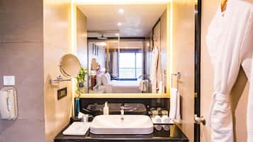 A modern bathroom with a large mirror, a sink, and a robe hanging on the wall.