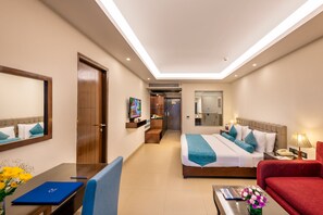A hotel room with a bed, a desk, a chair, a red sofa, a TV, and a bathroom visible through an open door. - Golden Tulip Goa Candolim (Candolim)