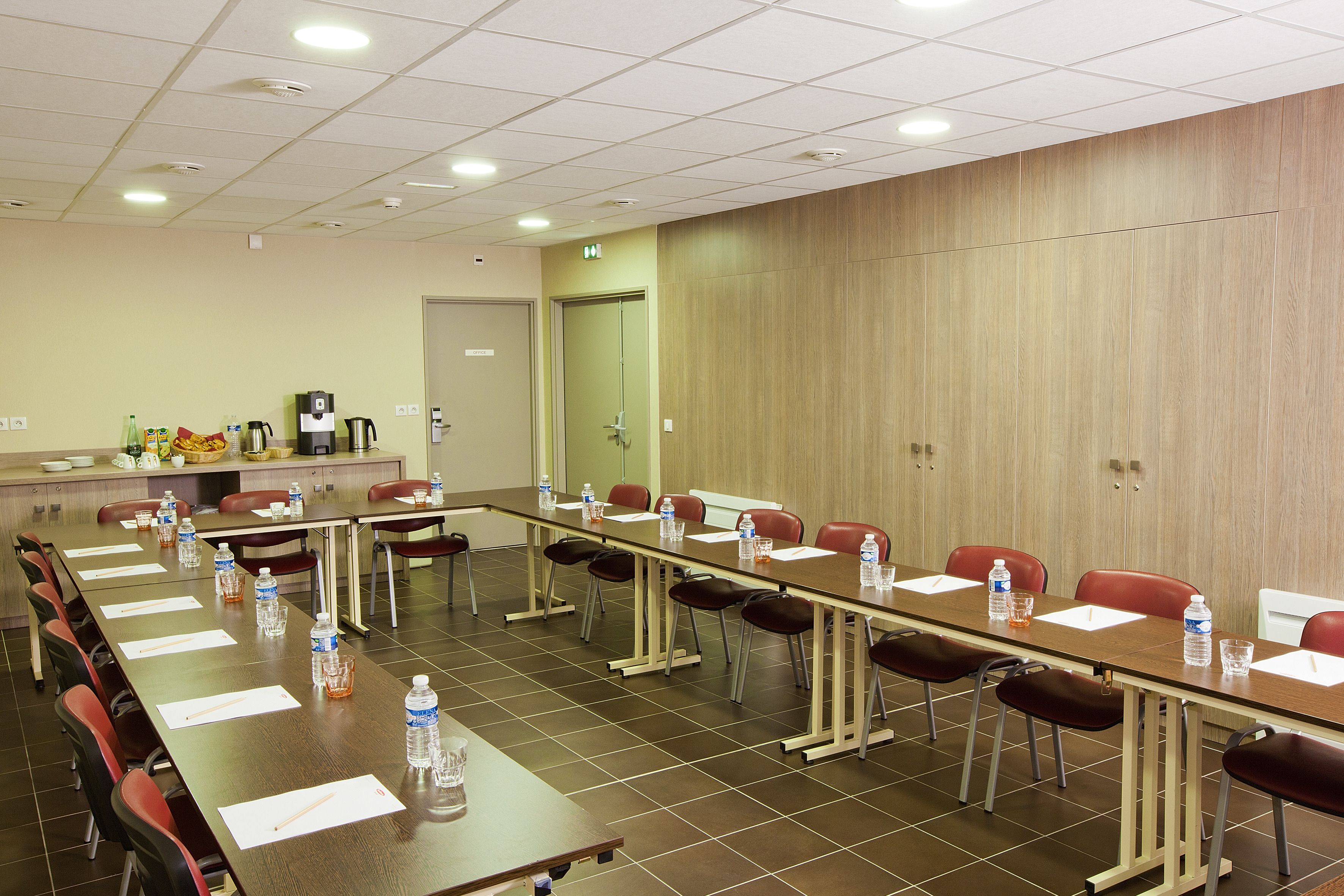 A conference room with a long table, chairs, water bottles, and a coffee station.