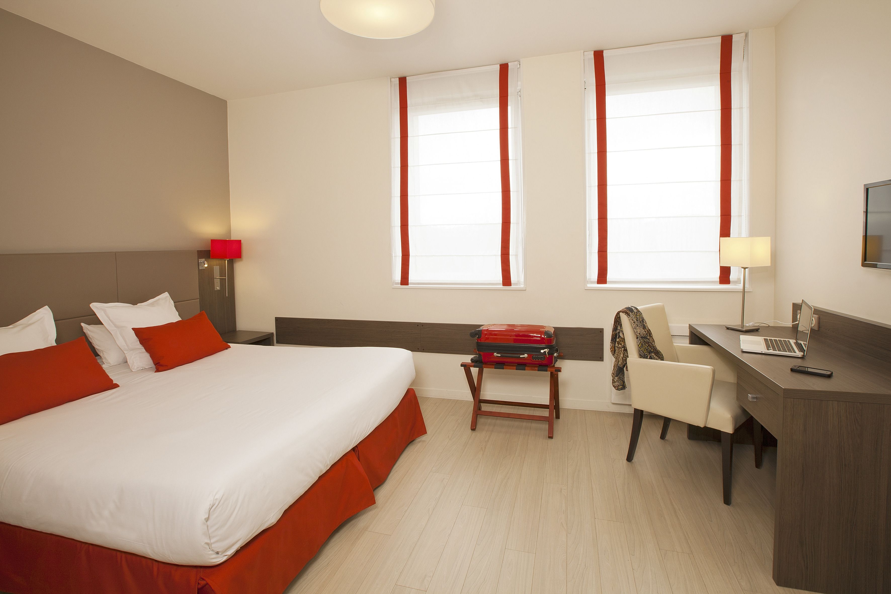 Una habitación de hotel con una cama grande, un escritorio y dos ventanas con cortinas rojas.