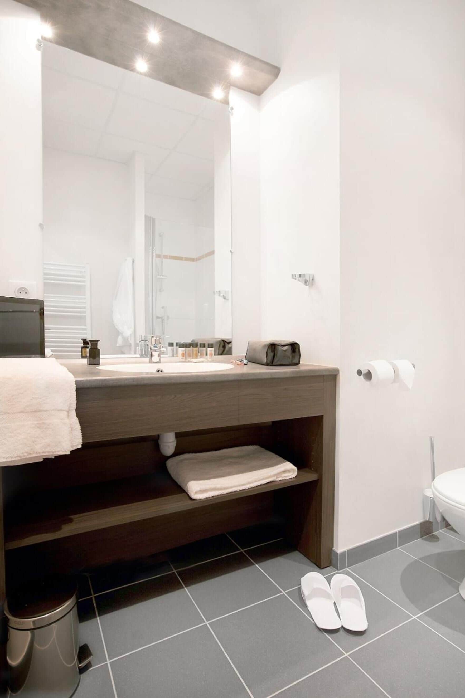 Un baño moderno con un espejo grande, un lavamanos, un perchero para toallas y un inodoro.