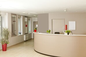 A reception area with a curved reception desk, potted plants, and a whiteboard on the wall. - Residhome Reims Centre (Reims)