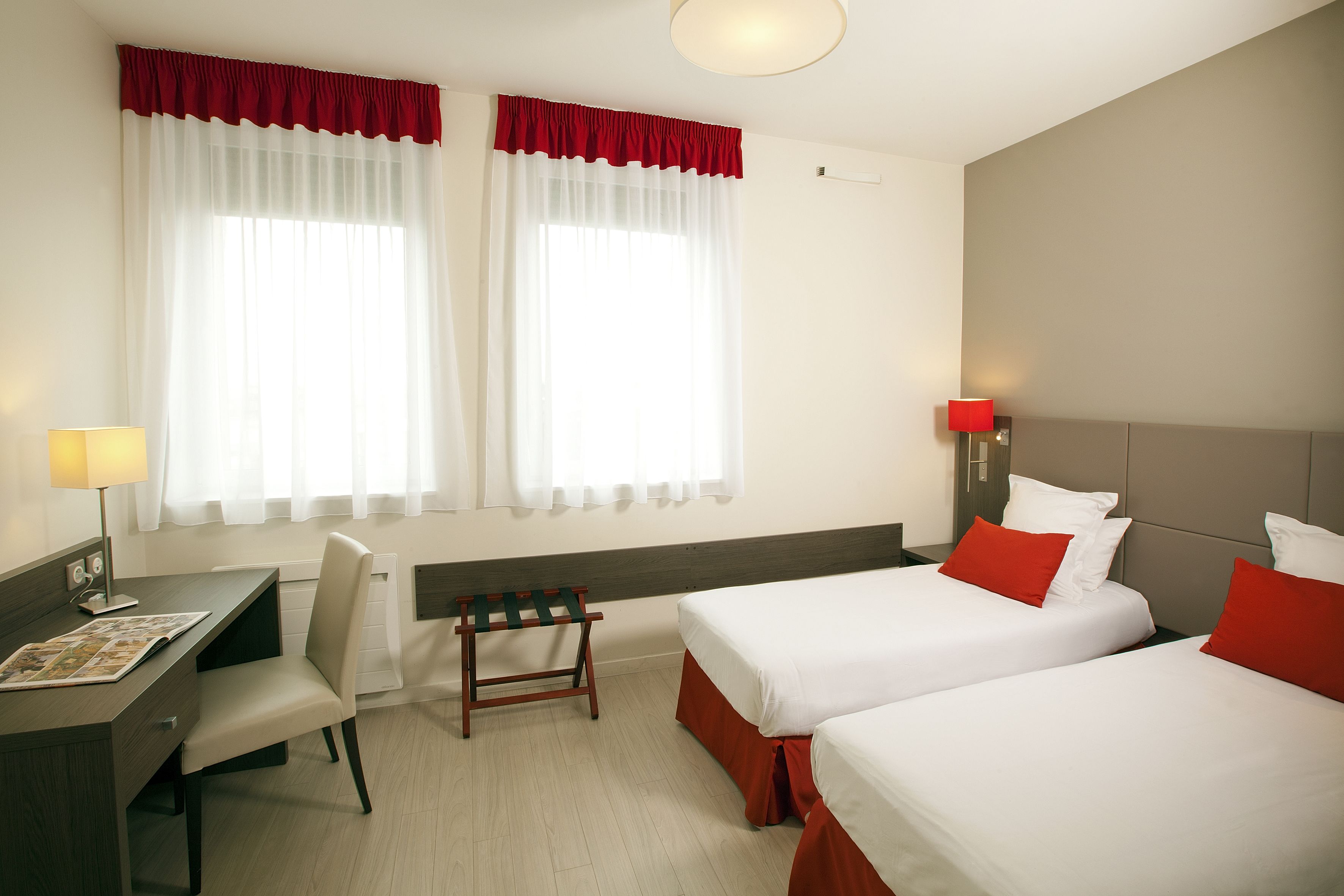 A hotel room with two beds, a desk, a chair, and a small table.