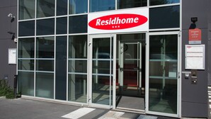 Un edificio moderno con una amplia fachada de vidrio, un letrero destacado de "Residhome" y una cámara de seguridad en la pared.